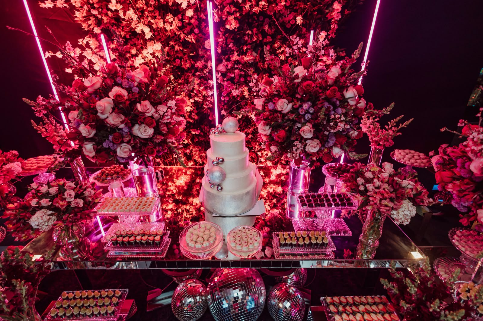 Mesa decorada com flores e iluminação rosa para festa de 15 anos